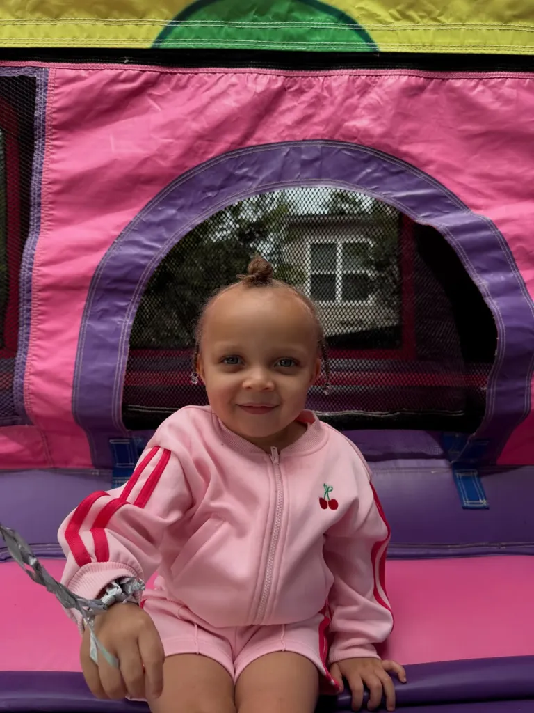 A young girl in a pink tracksuit sits in a bounce house.