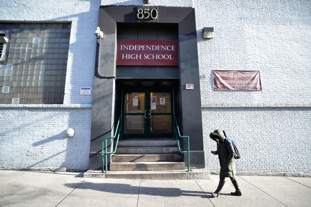 A student walks past the entrance of Independence High School, which has a sign for "ACADEMIC EXCELLENCE AND RESTORATIVE PRACTICES".