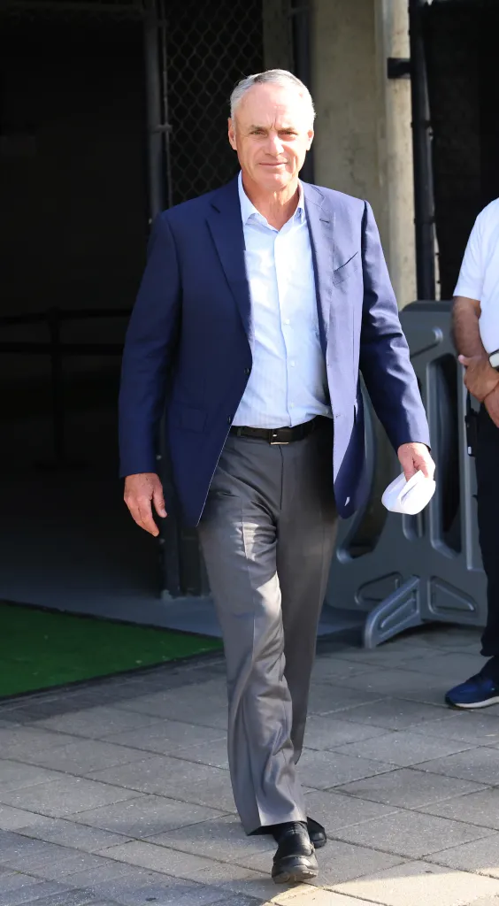 Commissioner Rob Manfred walking outdoors in a blue blazer and gray pants.