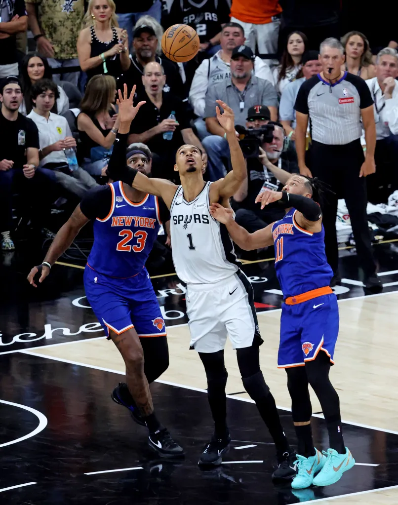 San Antonio Spurs forward Victor Wembanyama #1 reaches for a rebound between New York Knicks center Mitchell Robinson #23 and New York Knicks guard Jalen Brunson #11 during the 1st half.