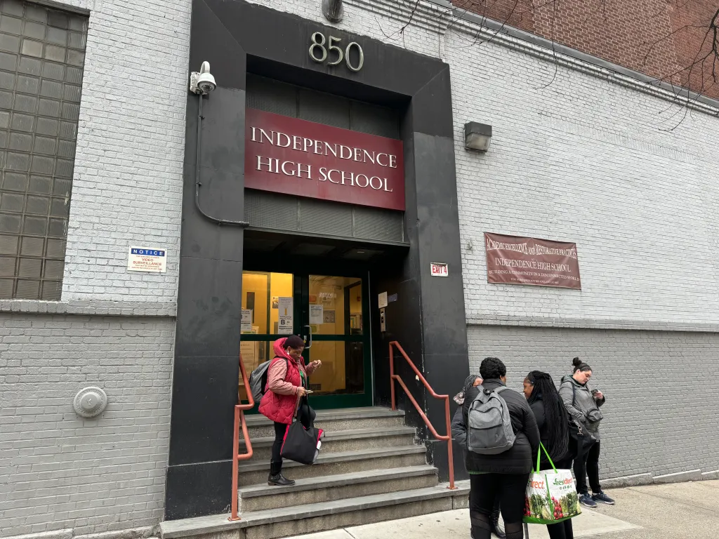 Students stand on the steps and sidewalk outside Independence High School, where a video surveillance notice is posted on the wall.