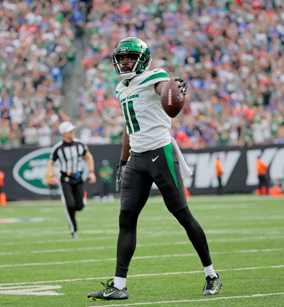 A football player in a green and white uniform holds a football on the field.