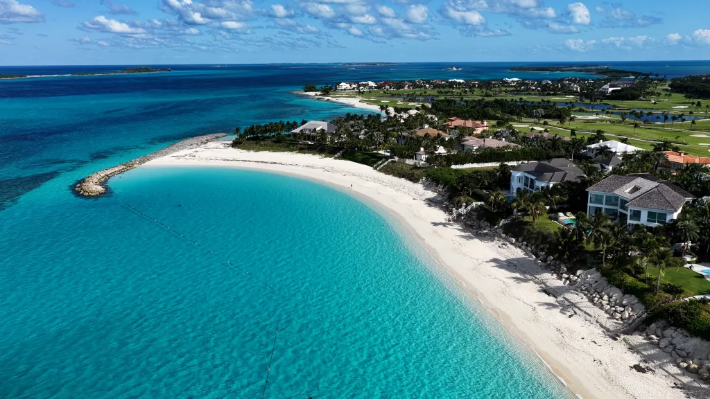 Aerial view of Cabbage Beach at Paradise Island in Nassau, Bahamas, showing the coastline with white sand, turquoise water, and luxury homes, hotels, and a golf course.