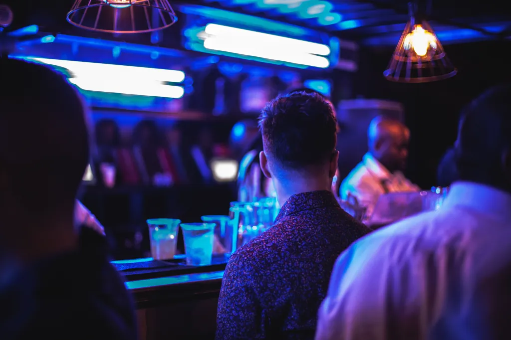 People standing at a bar in a dimly lit room with blue lights.