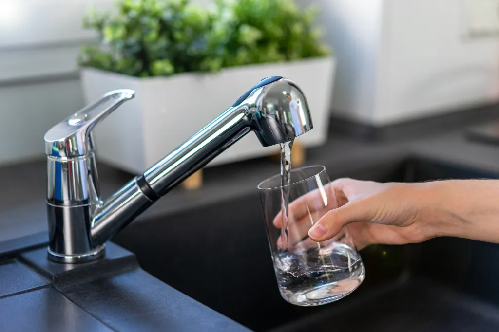 A woman's hand fills a glass with tap water in a kitchen sink.
