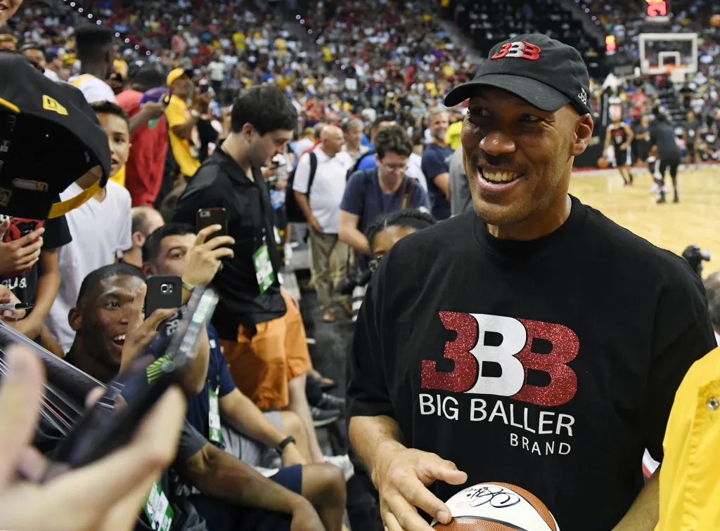 LaVar Ball smiling and holding a basketball while wearing Big Baller Brand merchandise.