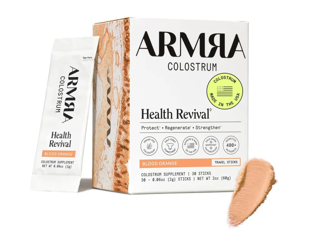 Armra Colostrum Blood Orange supplement box with a single serving packet and a pile of the powdered supplement.