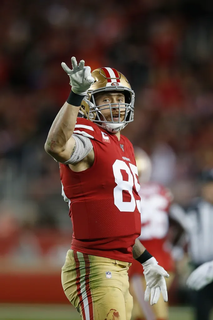 San Francisco 49ers tight end George Kittle wearing jersey #85, looks off to the right and signals with his left hand.