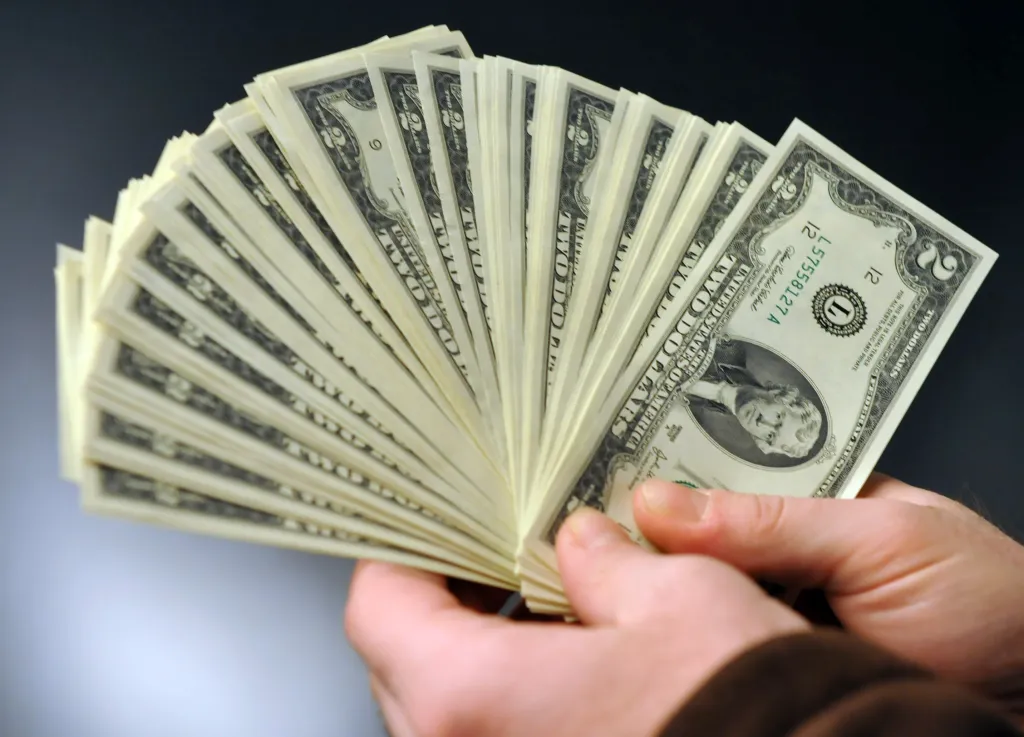 Hands holding and fanning out several two-dollar bills.