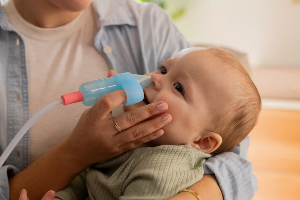 A baby having their nose cleaned with a nasal aspirator.