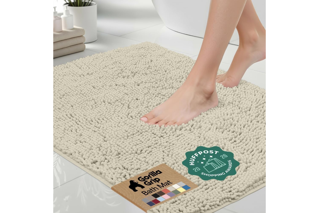 A person's bare feet stepping onto a cream-colored Gorilla Grip bath mat, with a HuffPost Shopping Awards badge.