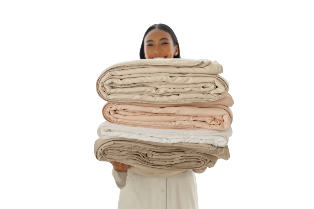 Smiling woman holding a stack of four Double Cocoon Mulberry Silk Filled Quilts in varying natural colors.
