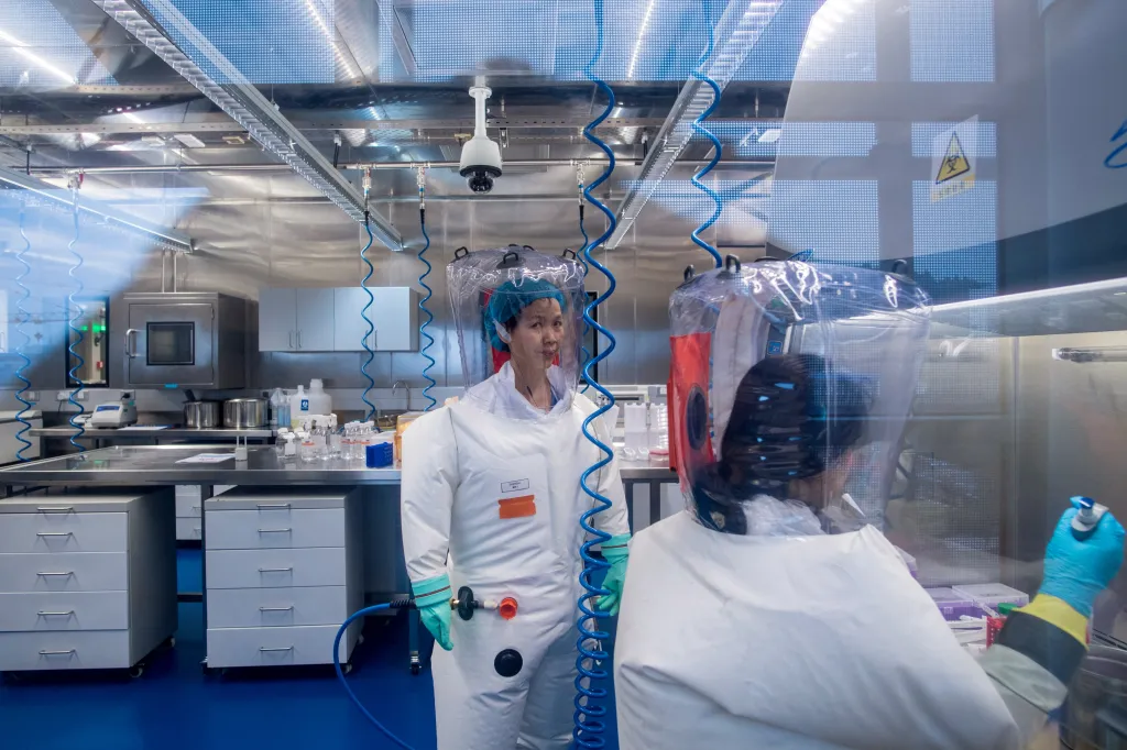 Virologist Shi Zhengli and another scientist wearing full white protective suits and clear helmet-like respirators in a P4 epidemiological laboratory.
