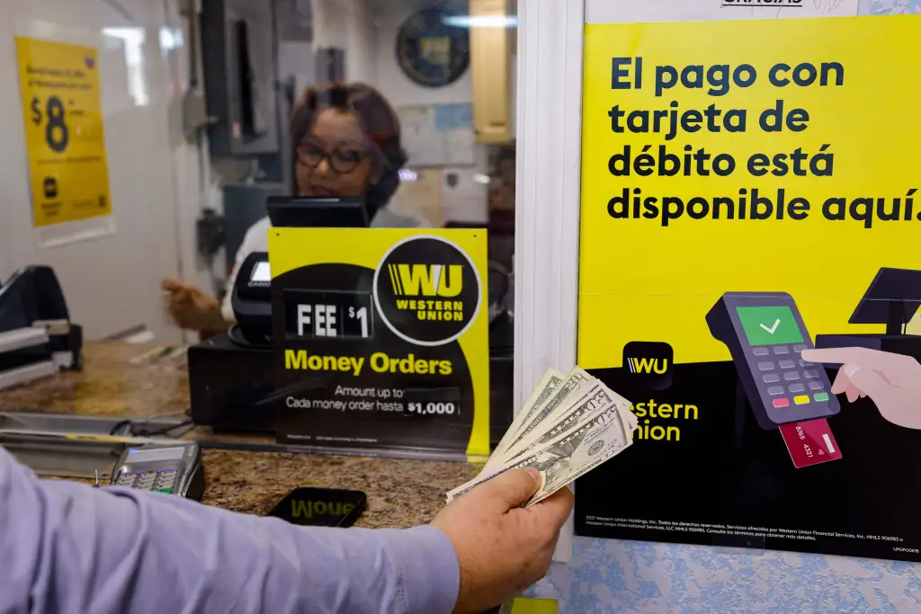 A customer holds cash next to Western Union signs at a check cashing window.