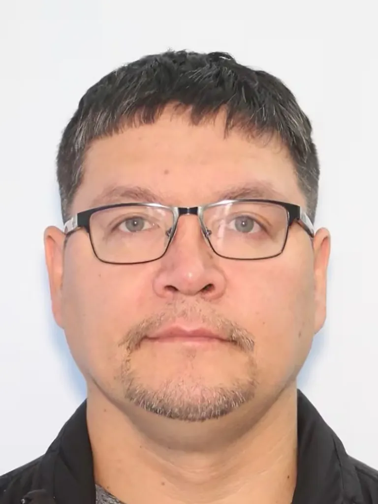 Headshot of Ulric Ulroan, a man with short, dark hair, graying temples, a mustache, and a goatee, wearing dark-rimmed glasses and a black jacket.