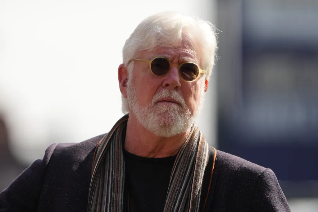 Mike Krukow, a man with a white beard and hair, wearing sunglasses and a scarf, looks ahead.