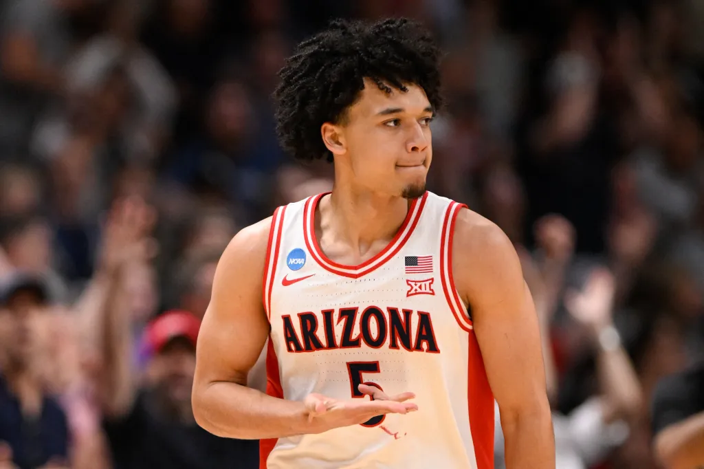 A basketball player in a white and red "Arizona 5" jersey looking to his right.