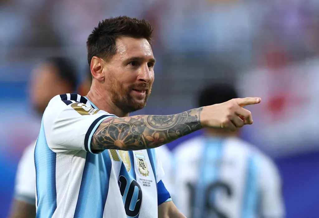 Lionel Messi in an Argentina jersey, smiling and pointing to the right.