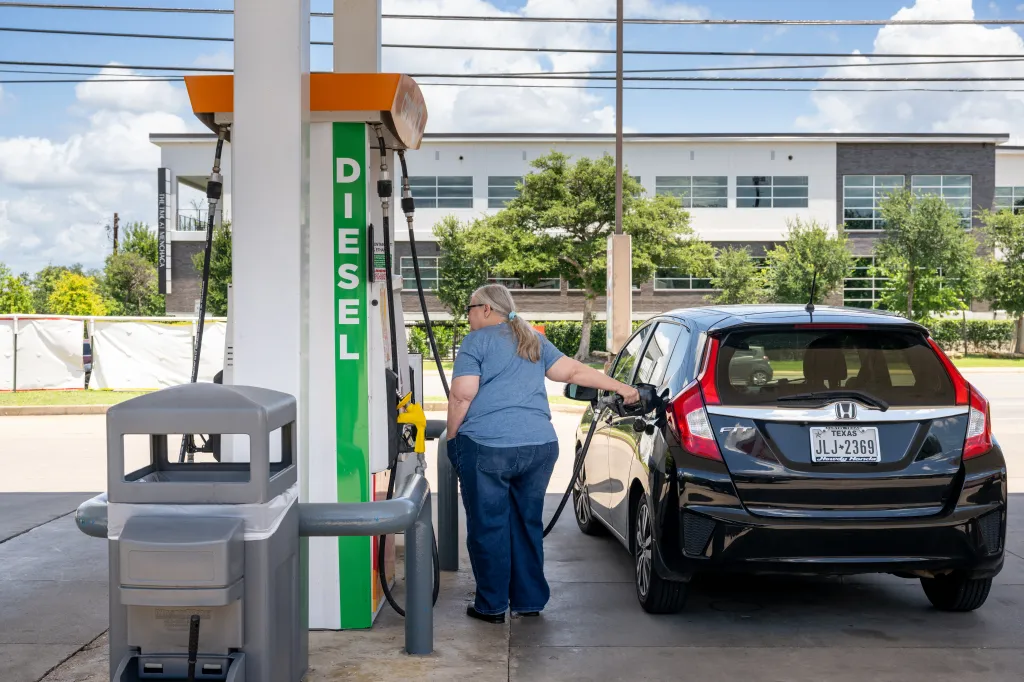 A person pumping diesel fuel into a black car at a Shell gas station.