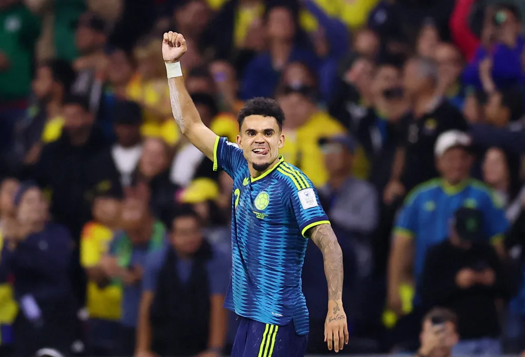 Colombia's Luis Diaz celebrates scoring a goal, with his right arm raised and left arm down, tongue out.