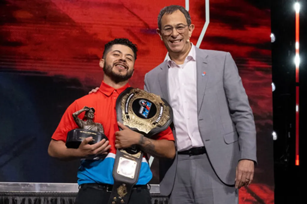 Richard Delcid, winner of the 2026 World's Fastest Pizza Maker award, holding his trophy and championship belt next to Domino's CEO Russell Weiner.