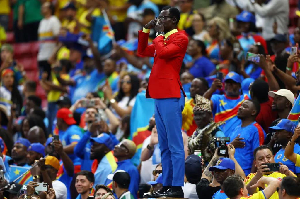 DR Congo fan Lumumba Vea standing in the stands, wearing a red jacket and blue pants.