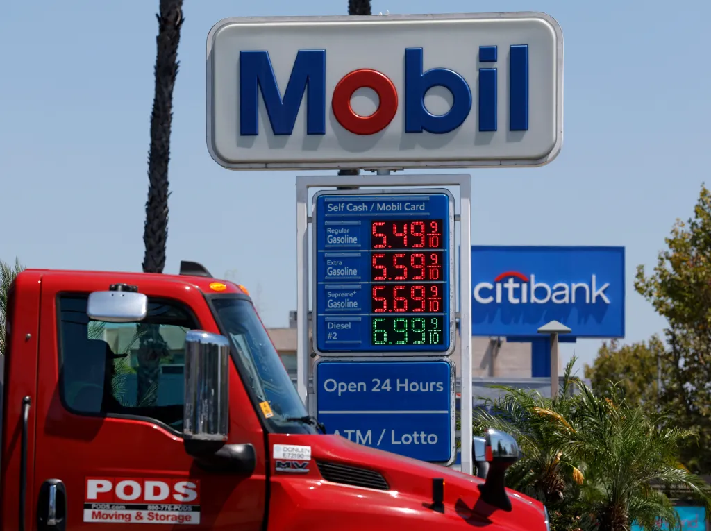 A Mobil gas station sign displaying prices of gasoline at $5.49, $5.59, and $5.69, and diesel at $6.99, with a red truck in the foreground.