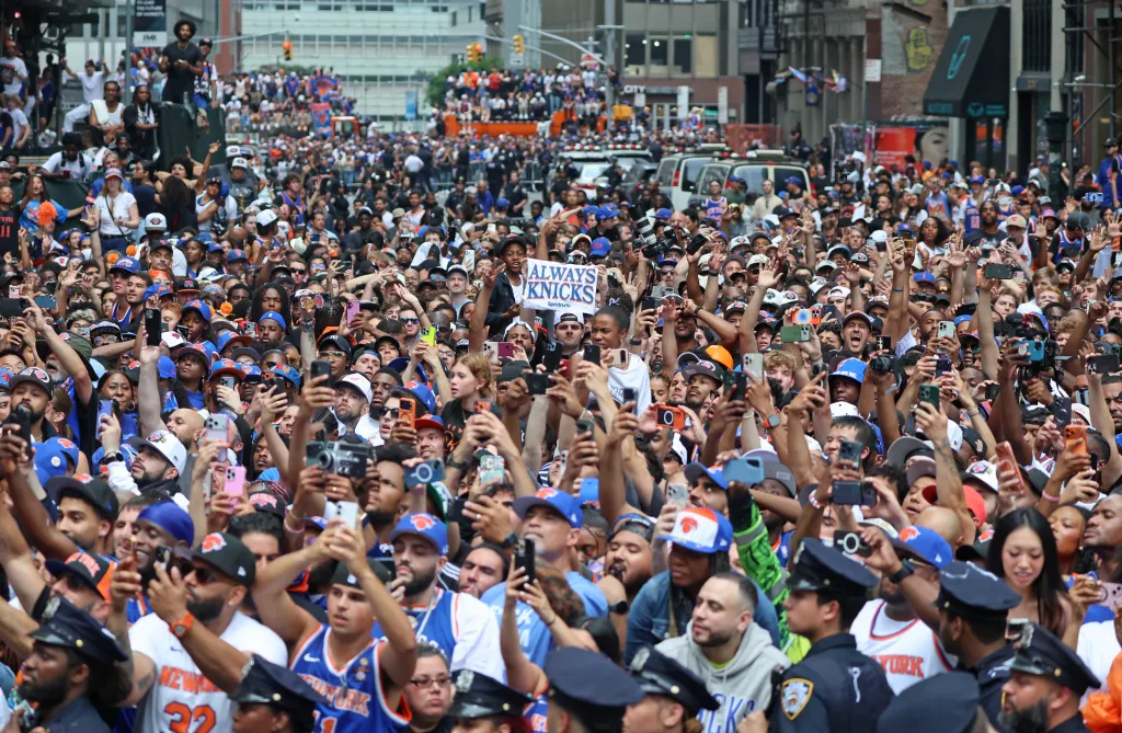 Crowds of fans wearing New York Knicks gear celebrate at a ticker-tape parade in Lower Manhattan.