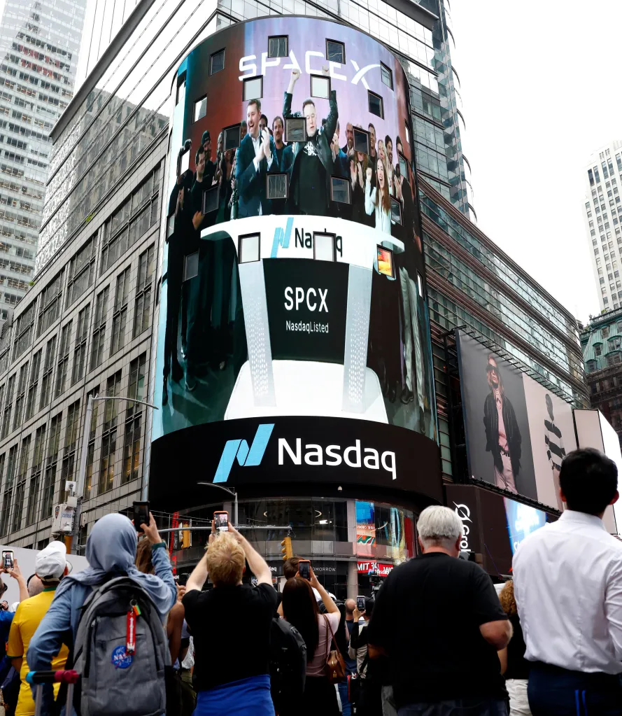 People watch a Nasdaq MarketSite screen in Times Square showing SpaceX branding and Elon Musk with his arms raised in celebration.