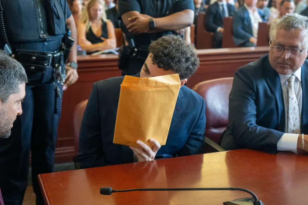 Accused murderer Luigi Mangione hides his face behind a manila envelope in court.