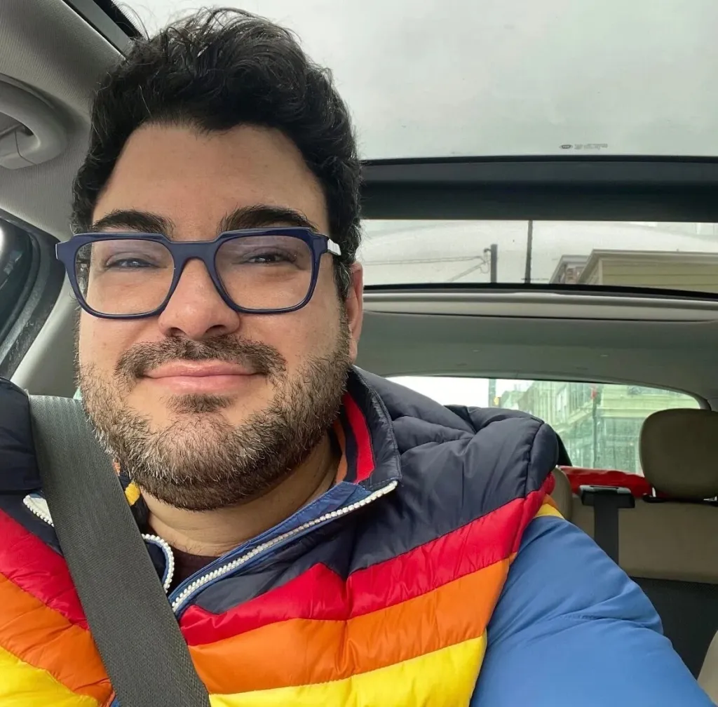 Travis J. Longo wearing glasses and a colorful puffer jacket while sitting in a car.