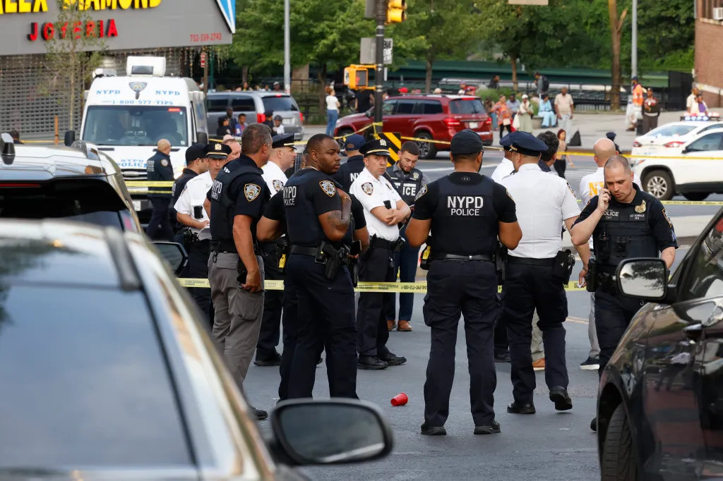 NYPD officers investigating a crime scene blocked off with yellow tape on a city street.