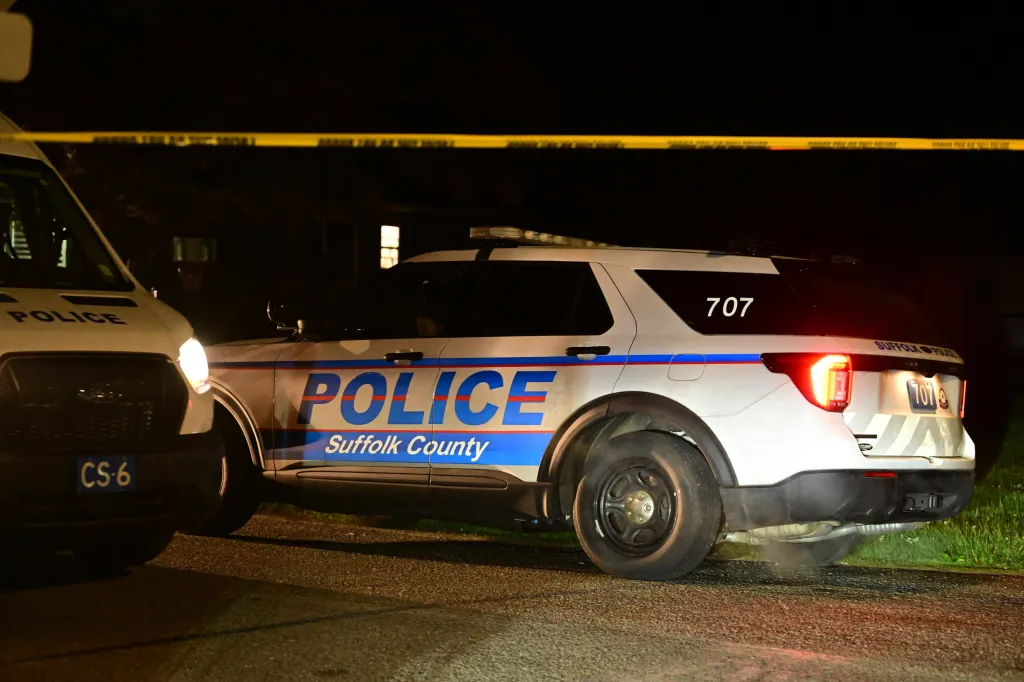 Suffolk County Police patrol car and Crime Scene Unit van parked on a street at night, with caution tape in the background.