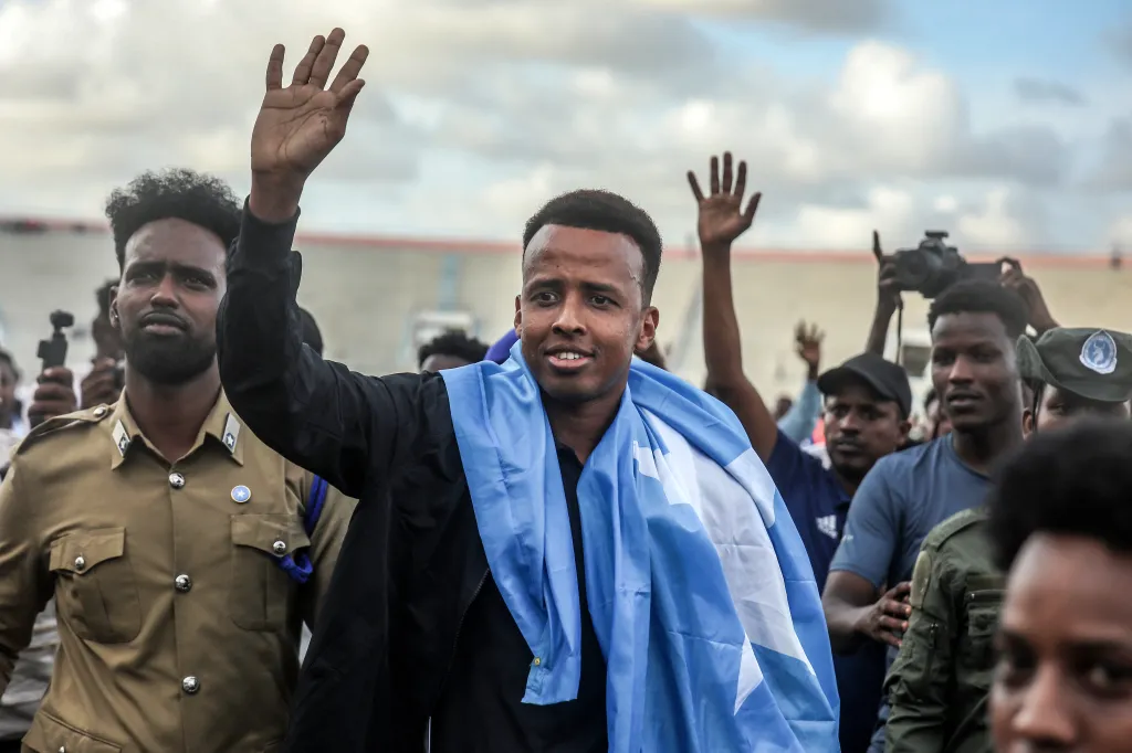 Somali international referee Omar Abdulkadir Artan waving to supporters with a Somali flag draped over his shoulders.