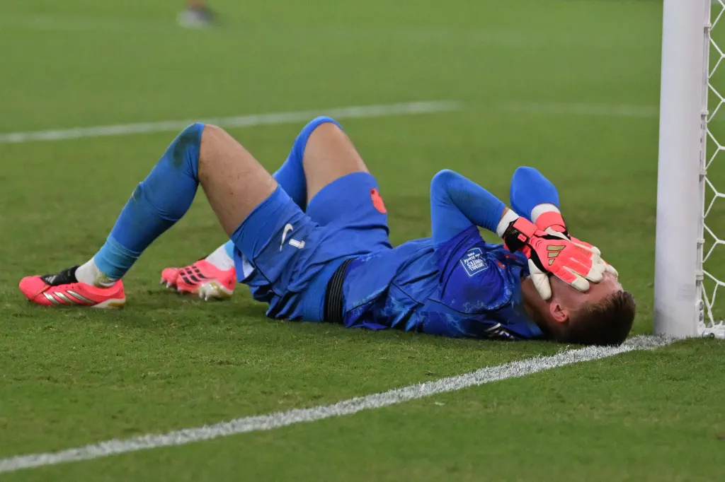 Bart Verbruggen, the Netherlands' goalkeeper, lying on the ground near the goalpost with his hands on his face after losing a shootout in a soccer match.