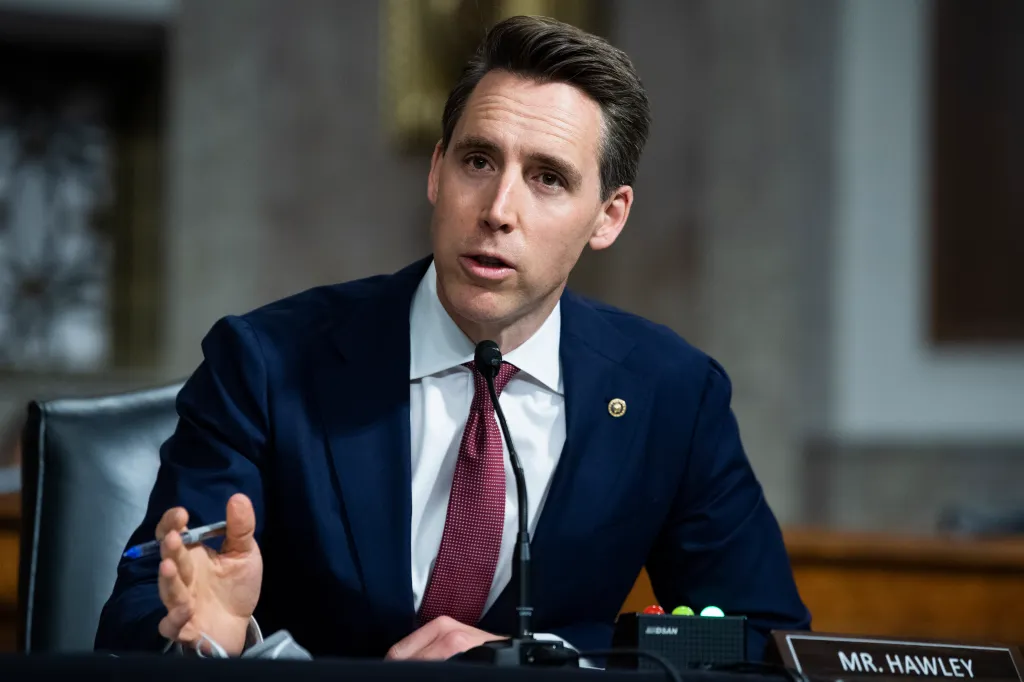 Senator Josh Hawley speaks at a hearing, wearing a navy suit and red tie.