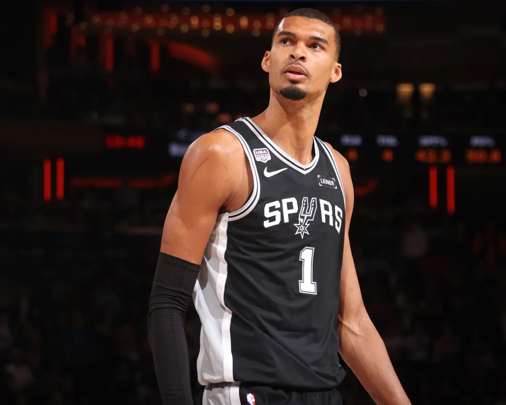 A male basketball player in a black and white Spurs jersey with number 1 looks up.