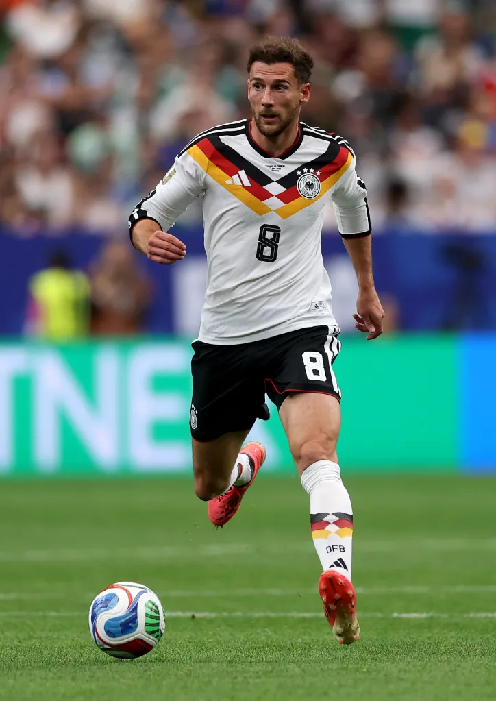 A German player in a white and black jersey with the number 8 on it, kicking a soccer ball.
