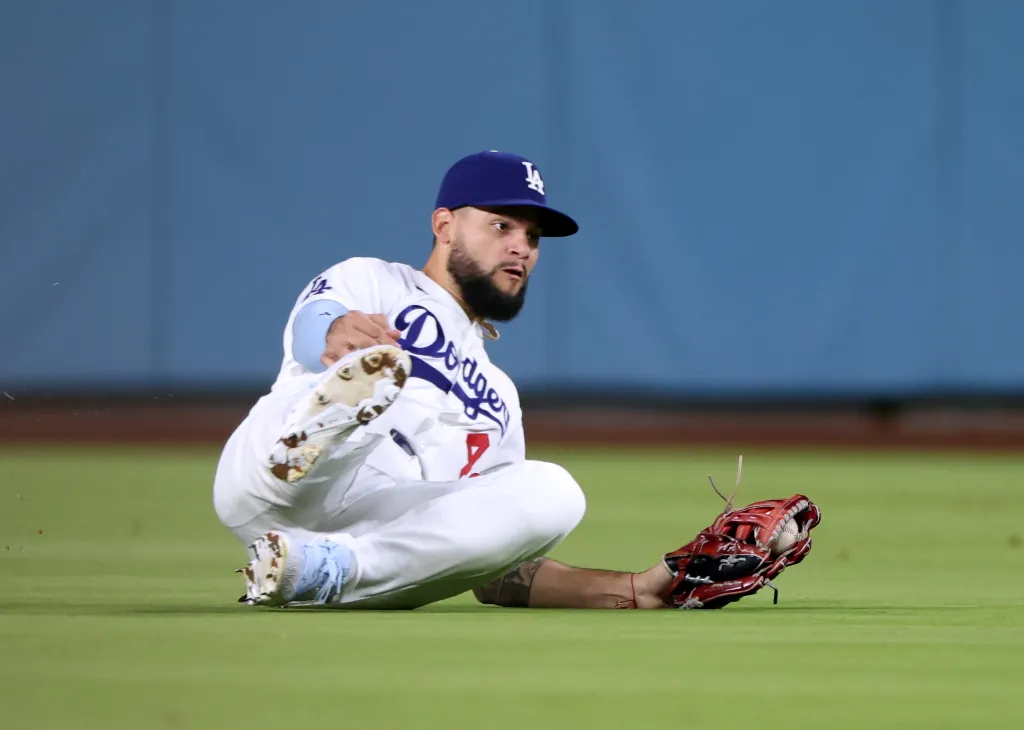 A baseball player from the Los Angeles Dodgers slides on the field with his glove reaching for the ball.