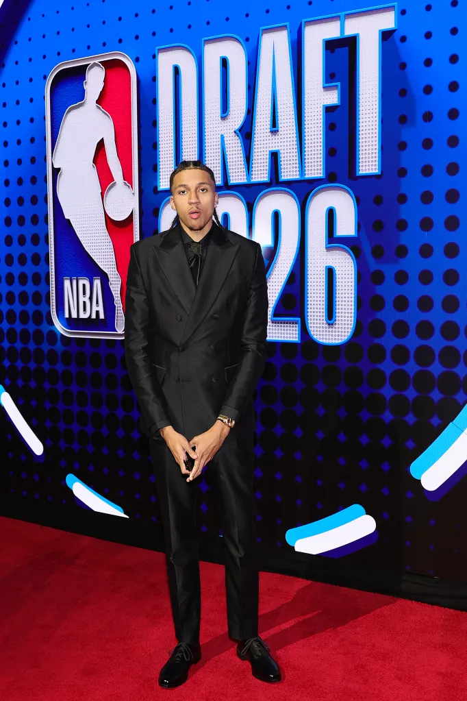 Man in a black suit standing on a red carpet in front of a “DRAFT 2026” sign.