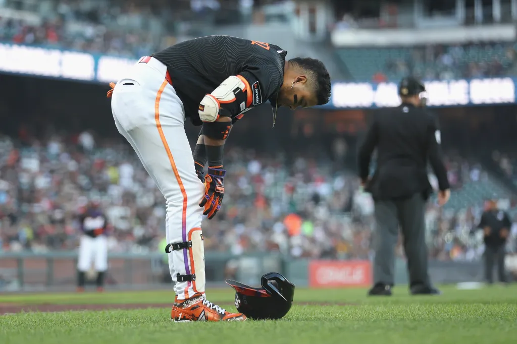 A baseball player bending down on the field with his helmet at his feet during a game between the Athletics and the San Francisco Giants.