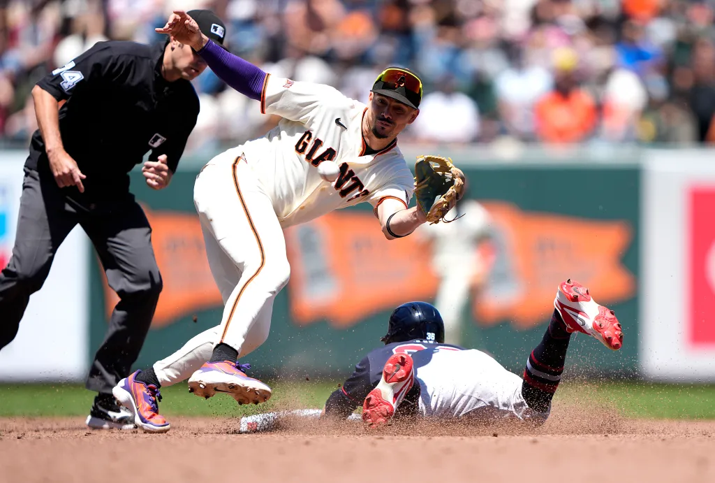 A Giants player attempts to tag out a Braves player sliding into base as an umpire looks on.