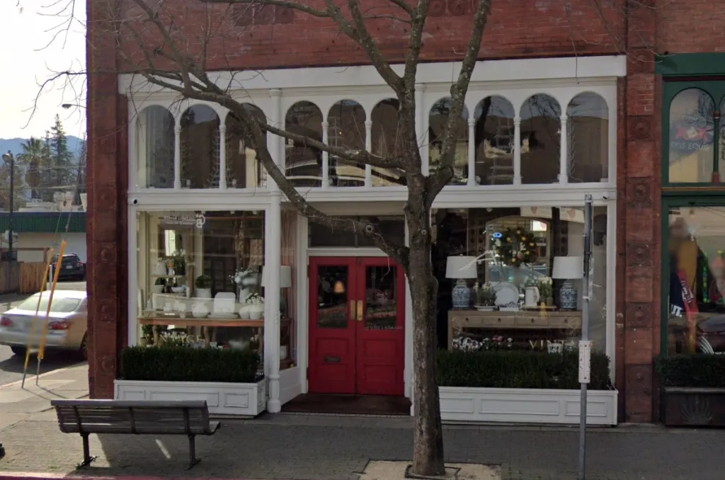 Storefront of Napa Valley Vintage Homes with large display windows, red double doors, and a tree in front.