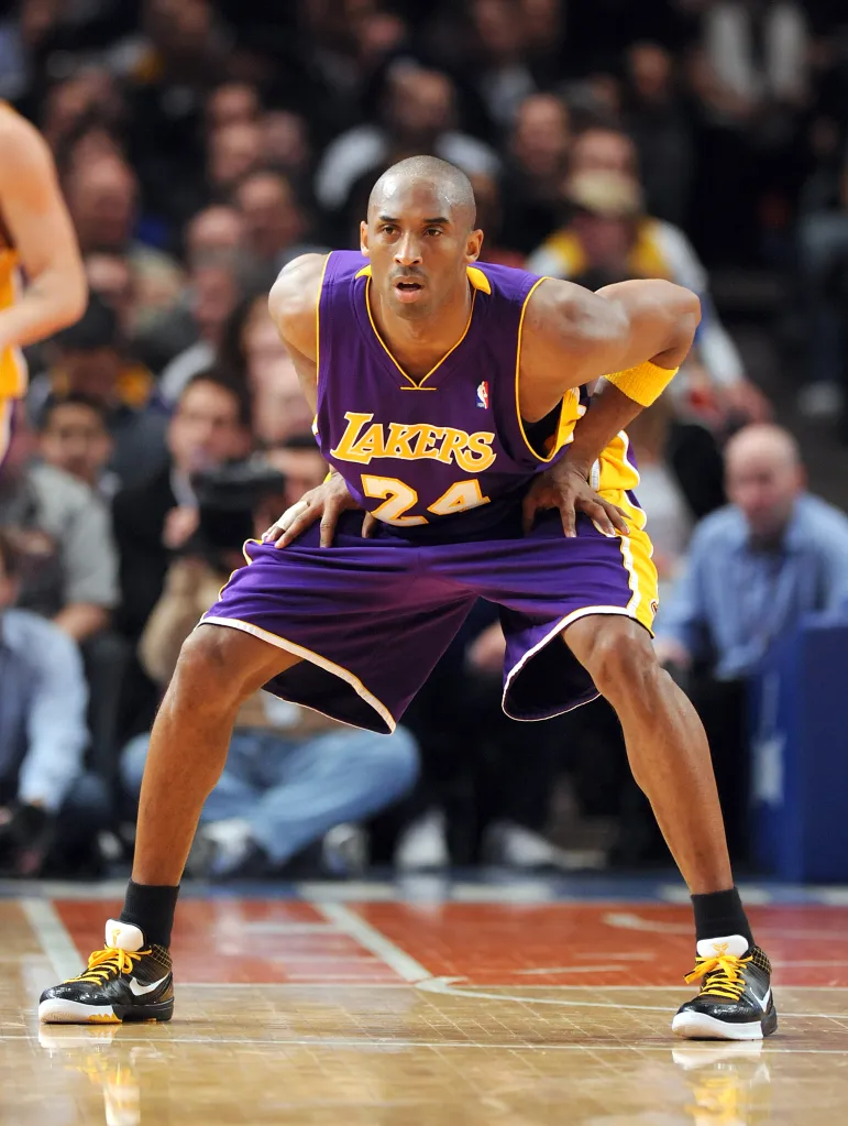 Kobe Bryant in Lakers uniform with "24" in a defensive stance on a basketball court.