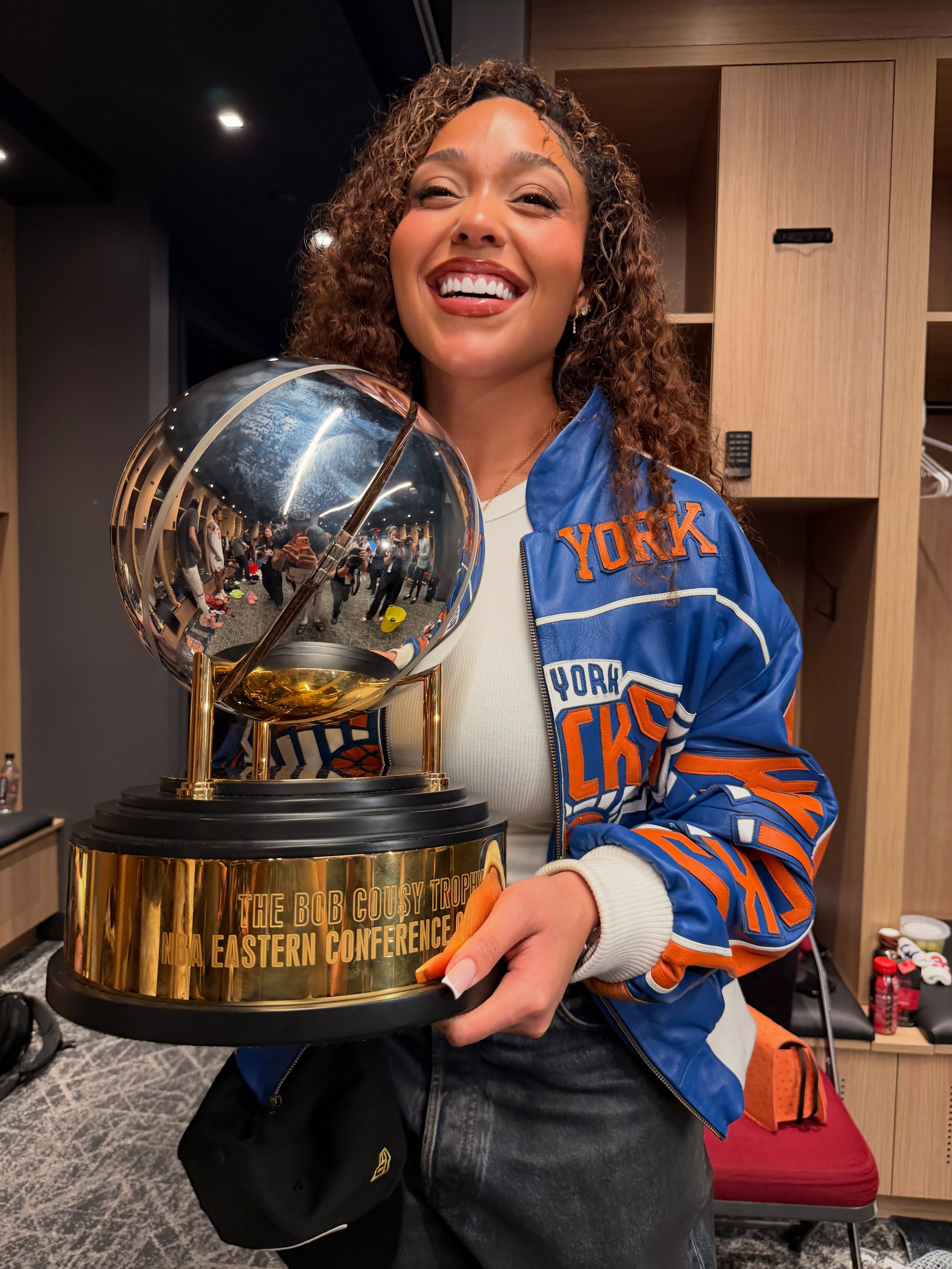 Jordyn Woods holding the NBA Eastern Conference Finals trophy while wearing a blue and orange jacket.