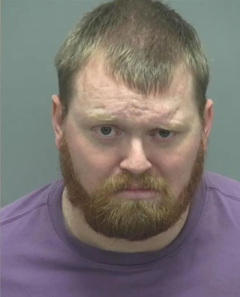 Mugshot of a man with a reddish-brown beard and short blonde hair, wearing a purple shirt.