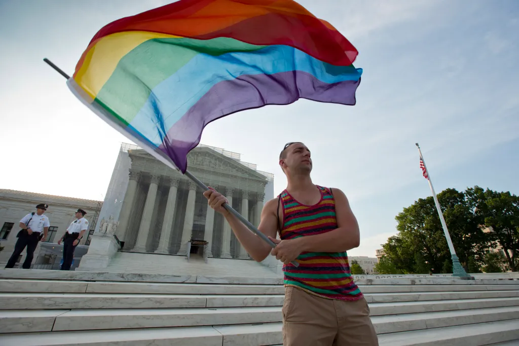 A man waving a rainbow flag in front of the US Supreme Court building.