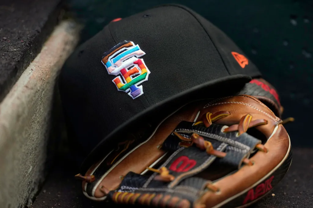A black San Francisco Giants baseball cap with a rainbow "SF" logo rests on a baseball glove.