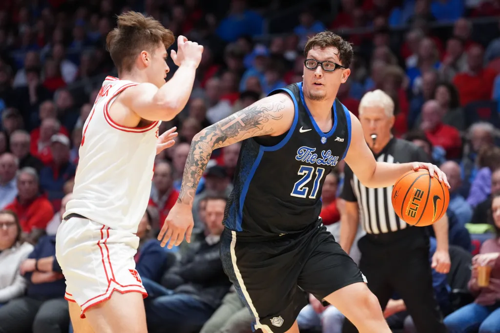 A player from Saint Louis with the number 21 dribbles a basketball while being guarded by a Dayton player.