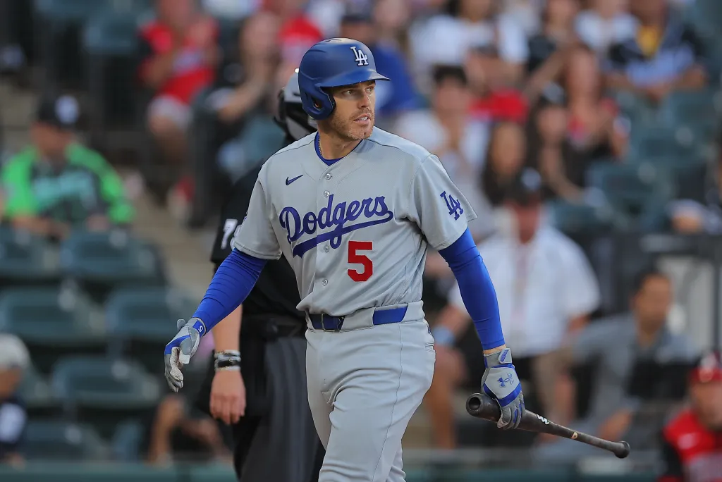 A baseball player in a gray uniform and blue helmet holds a bat while looking to the right.